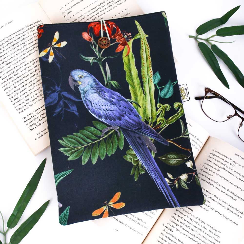 Book sleeve with a blue parrot and floral design on a white surface with books and glasses.