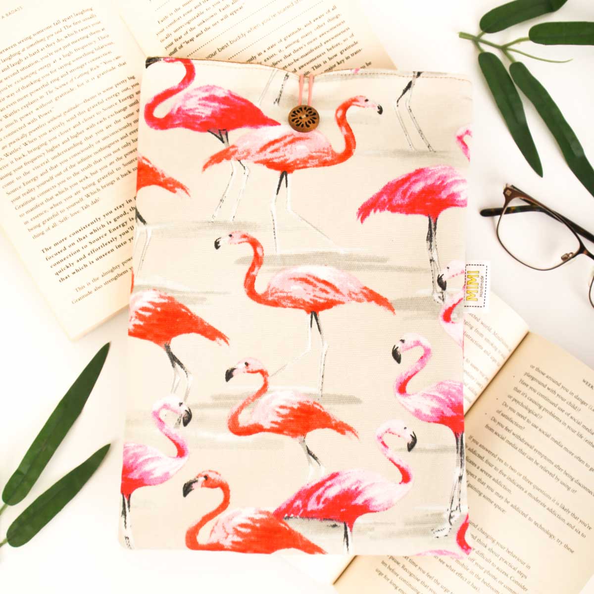 Flamingo-patterned pouch on a surface with an open book and glasses.