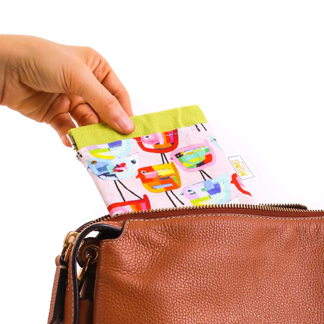Hand opening a brown leather bag with a colorful patterned pouch inside.