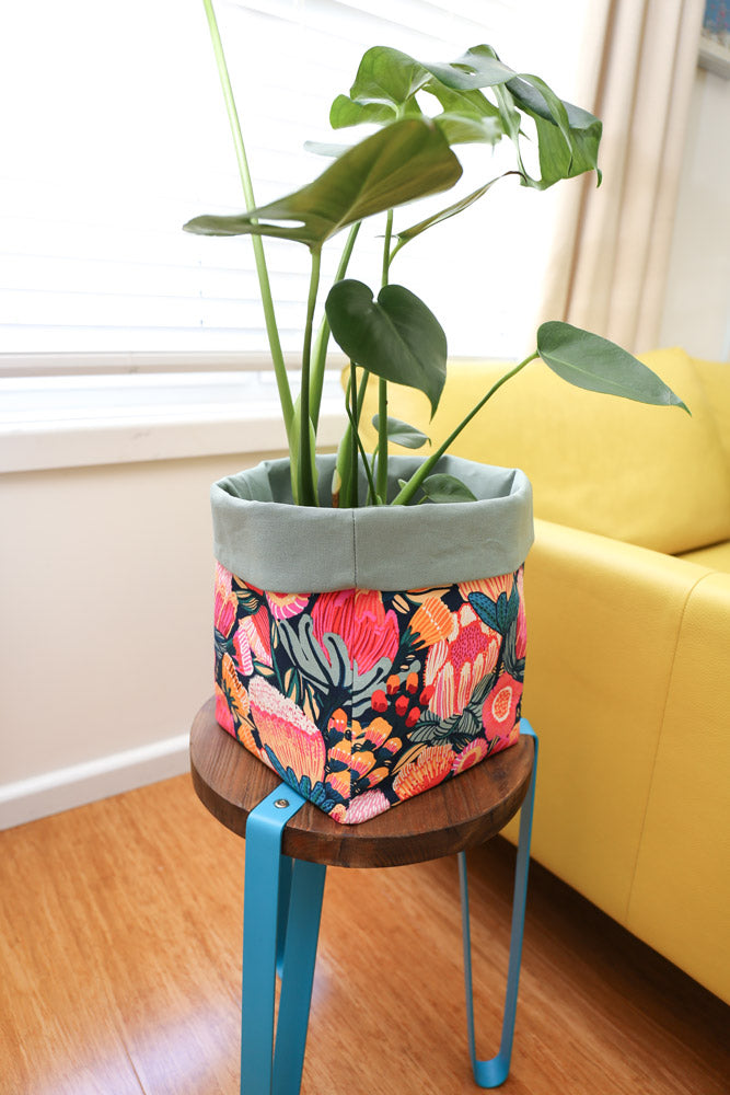 pink protea blossom large fabric pot plant holder on stool next to yellow sofa 